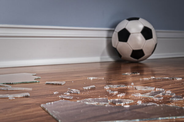 Replacement Windows Kewanee IL, Pieces of glass from a broken window pane on the wood floor inside a home with a soccer ball in in the background